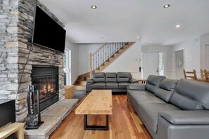 Una sala de estar moderna con chimenea de piedra, sofás de cuero, una mesa de centro de madera y una escalera.