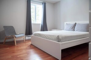 Un dormitorio con una cama, una silla, una mesita de noche y una ventana con cortinas.