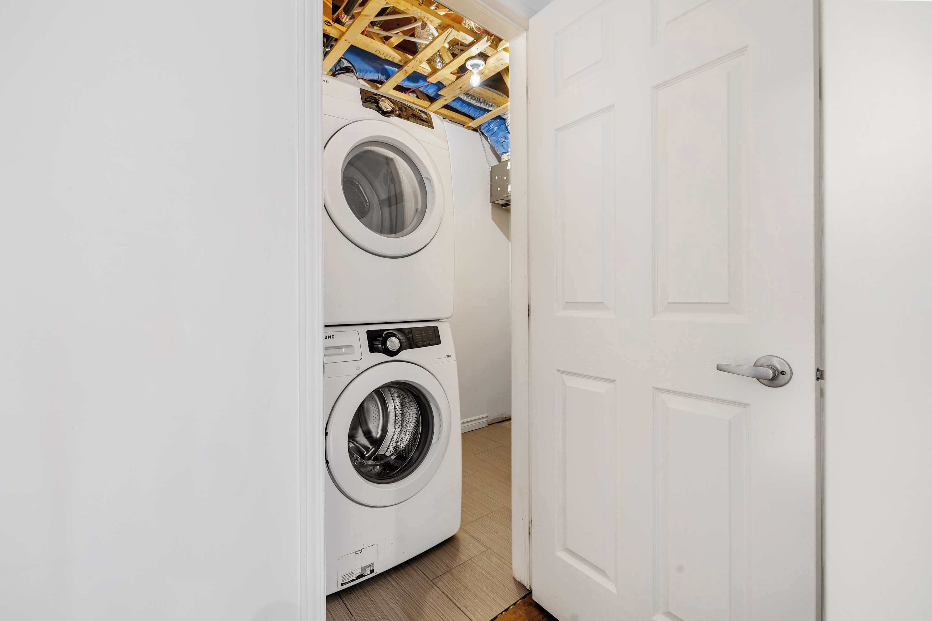 A laundry room with two front-loading washing machines, a wooden ceiling, and a white door.