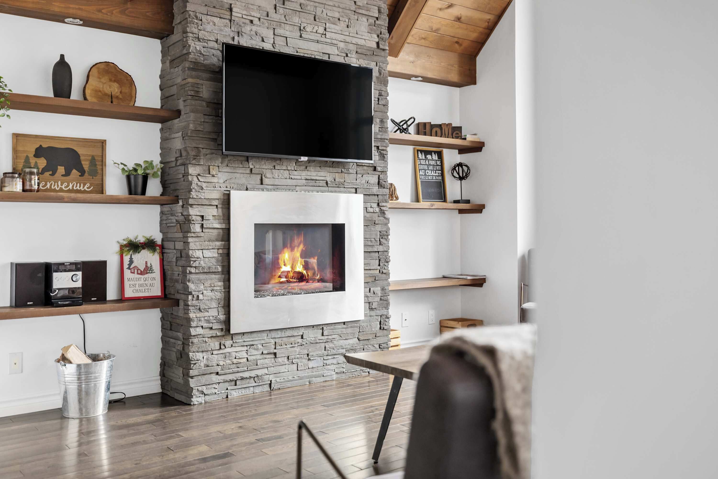 Un salon moderne avec une cheminée en pierre, des étagères en bois et un téléviseur fixé au mur.