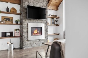 Moderni olohuone, jossa on kivinen takka, puuhyllyt ja seinälle asennettu televisio.