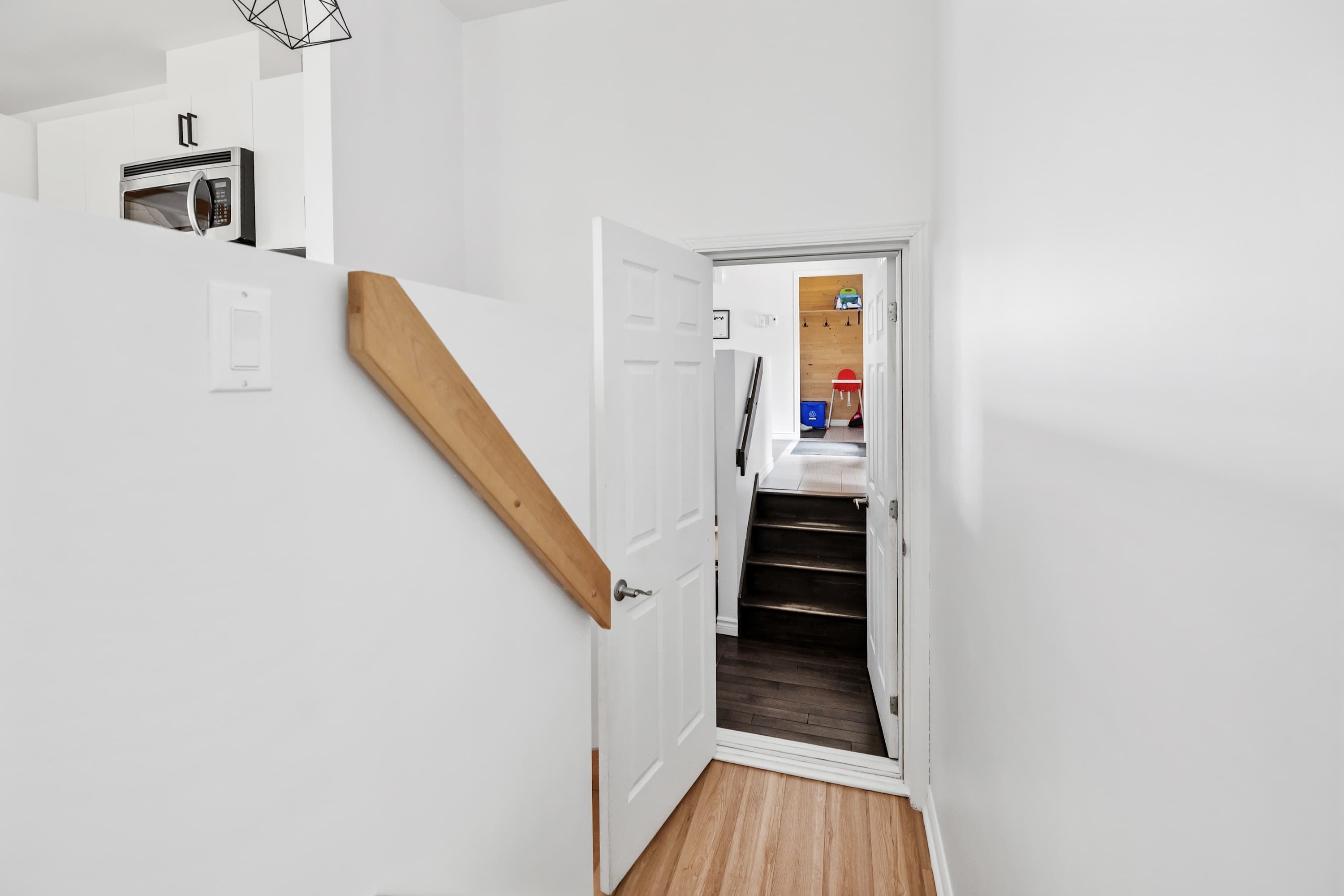 A staircase leading to a room with a microwave, a door with a handle, and a wooden floor.