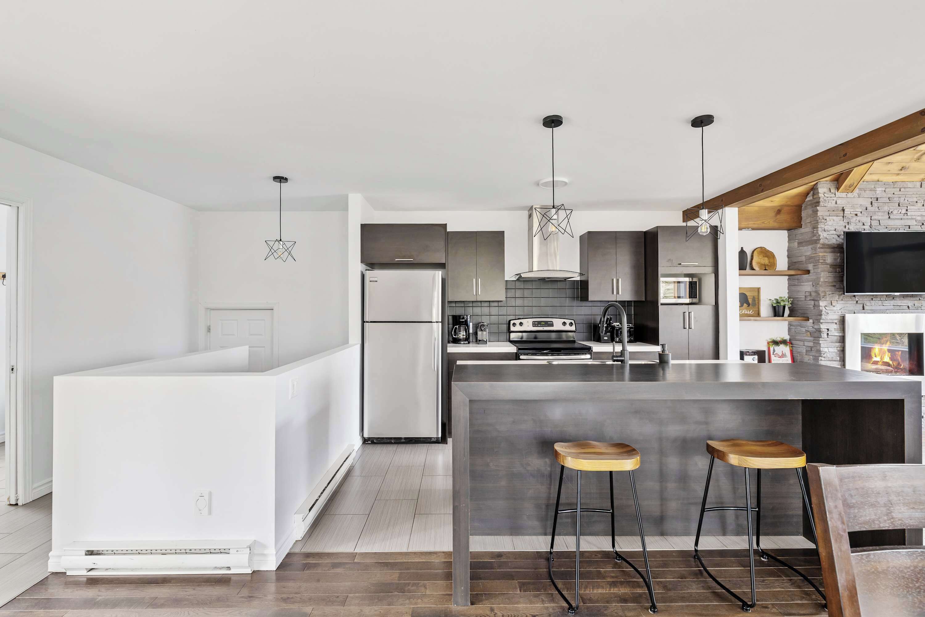 A modern kitchen with a central island, bar stools, and a stone fireplace.
