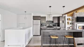A modern kitchen with a central island, bar stools, and a stone fireplace.