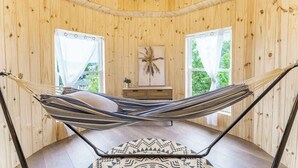 A hammock in a wooden room with a chandelier, a small table, and a painting on the wall.
