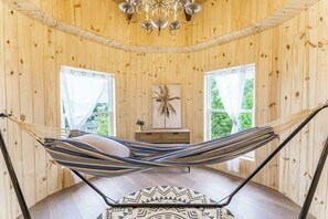Una hamaca en una habitación de madera con un candelabro, una mesita y un cuadro en la pared.