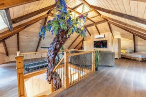 Interior de madera con una escalera, un arreglo floral colgante, un televisor y un sofá.