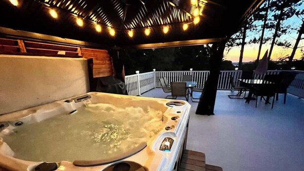 A hot tub with a wooden deck and a white fence in the background.