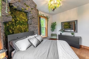 Una camera da letto con un letto, una cassettiera, uno specchio e una finestra con vista sul verde.
