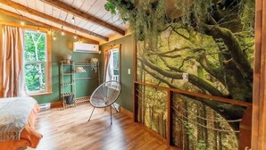 A room with a bed, a chair, a shelf with plants, and a wall mural of a forest.