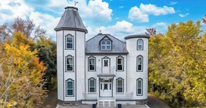 Una casa grande de dos pisos con una torre central, múltiples ventanas y un porche delantero.