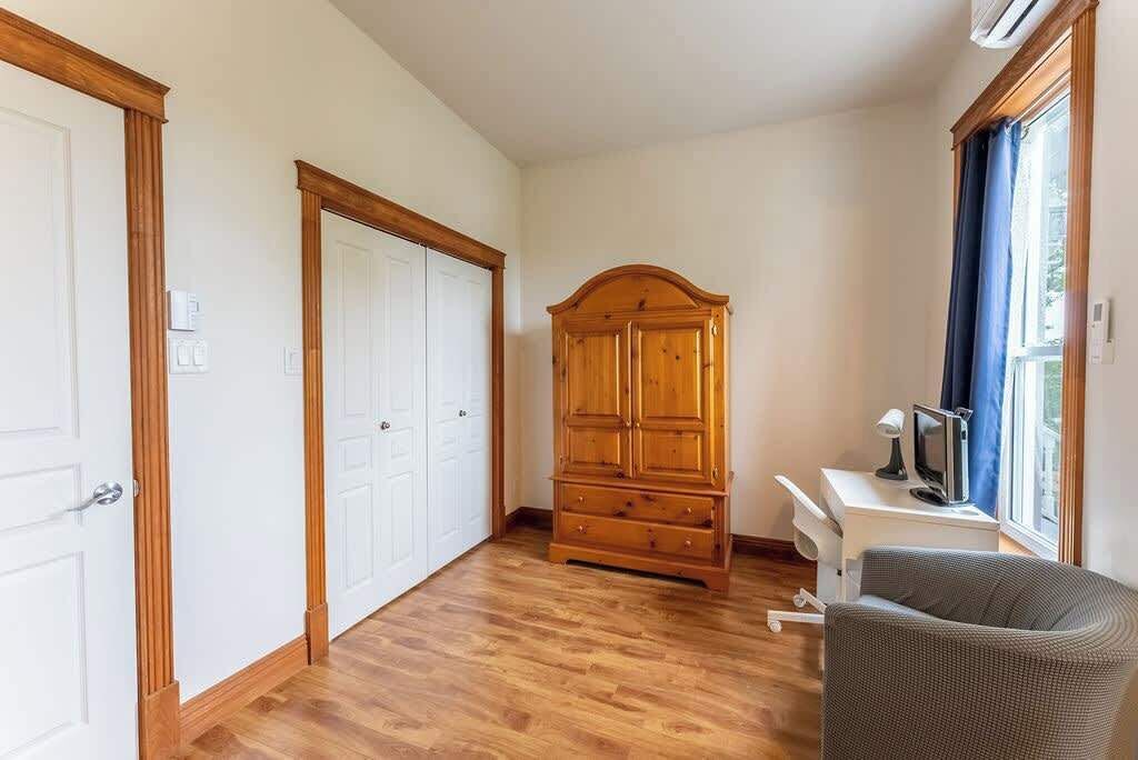 Une pièce avec un plancher en bois, une grande armoire en bois, un bureau avec une chaise et une fenêtre avec des rideaux.