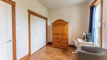 Une pièce avec un plancher en bois, une grande armoire en bois, un bureau avec une chaise et une fenêtre avec des rideaux.