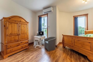 Un dormitorio con un armario de madera, un escritorio con computadora, una silla gris y una cama con cabecera de madera.