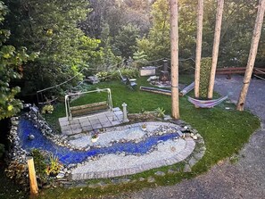 Un jardín con un sendero de piedra, un espacio de descanso y una pequeña fuente de agua.