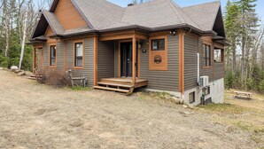 A two-story log cabin with a front porch, a covered outdoor seating area, and a small attached shed.