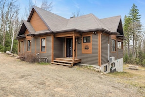 A two-story log cabin with a front porch, a covered outdoor seating area, and a small attached shed. - Nocturne  Spa Prive, 3 Chambres, 2 SDB  Domaine Boreal (Petite-Rivière-Saint-François)