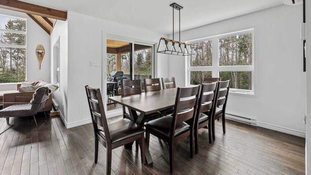 A dining area with a wooden table and chairs, large windows, and a ceiling fan.