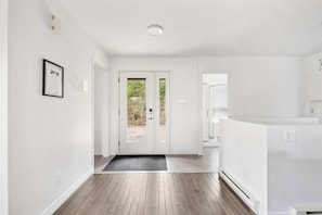 A modern interior with a wooden floor, white walls, a framed certificate on the wall, and a double door leading outside. - Nocturne  Spa Prive, 3 Chambres, 2 SDB  Domaine Boreal (Petite-Rivière-Saint-François)