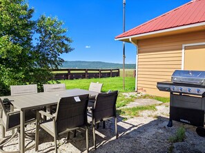 En uteplats med ett bord och stolar, en grill och utsikt över en inhägnad betesmark.