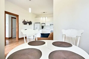 Un comedor con una mesa blanca, cuatro sillas y una silla blanca con un respaldo decorativo.