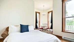 Quarto com cama grande, mesa de jantar com cadeiras, lustre e janela com vista.