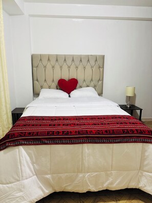 A bed with a tufted headboard, a red heart-shaped pillow, white bedding, and a patterned red and black throw blanket. - Magahousecusco (Cusco)