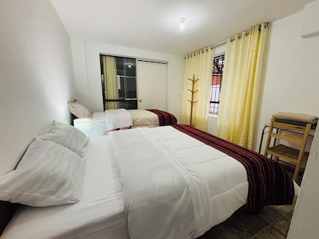 A bedroom with two beds, a window with yellow curtains, a wooden chair, and a door with a glass panel.. Magahousecusco