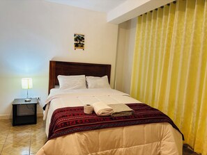 Ein Hotelzimmer mit Bett, Nachttisch mit Lampe, Wandbild und gelber Vorhang.