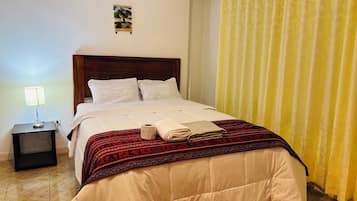 Una cama bien tendida con una colcha de diseño rojo y negro, una mesita de noche con una lámpara y un cuadro colgado en la pared.