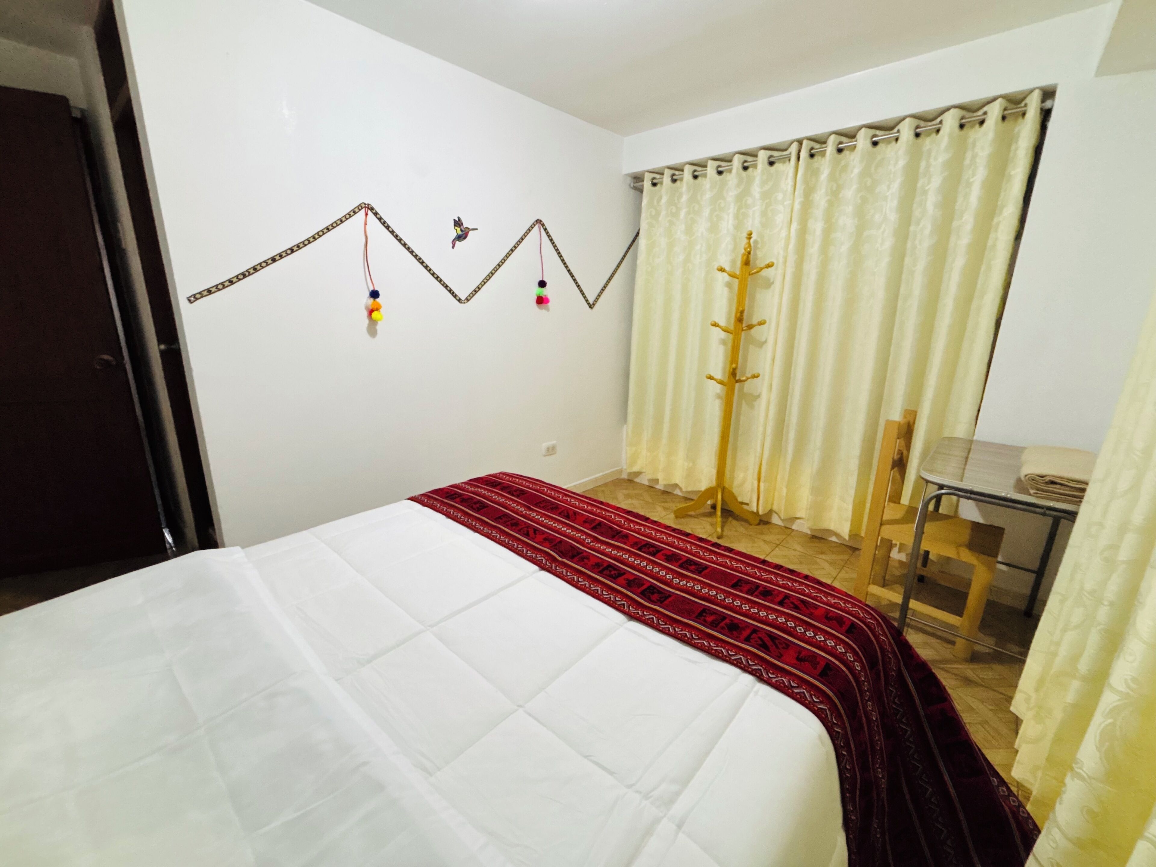 Un dormitorio con cama, escritorio, silla, perchero y ventana con cortinas.