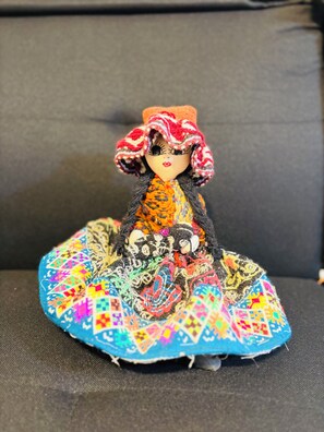 A doll with a colorful dress and a patterned hat sitting on a fabric-covered surface.