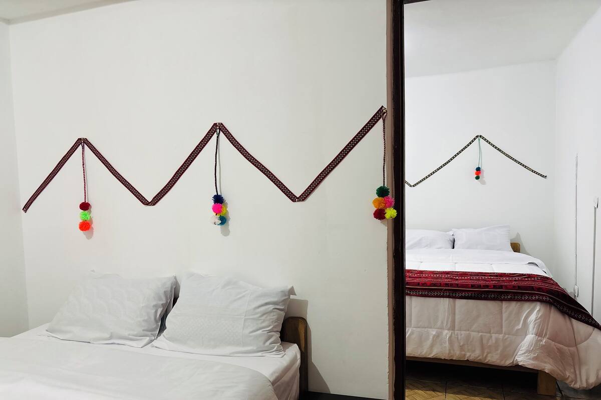 Una habitació amb un llit, un mirall i una decoració mural amb borla penjada.