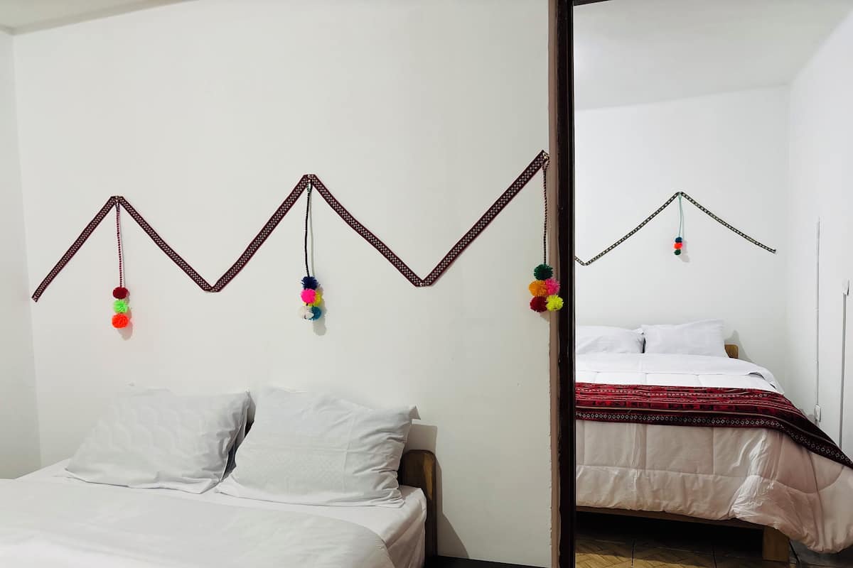 A room with a bed, a mirror, and a wall decoration with hanging tassels.