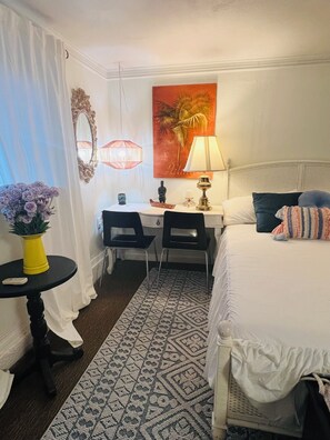 Et hotelværelse med en seng, et skrivebord med to stole, en lampe, et billede og et lille bord med en vase.