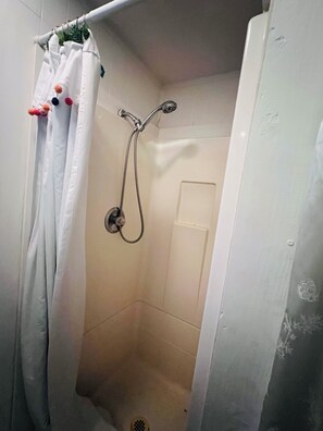 A shower with a handheld showerhead, a shower curtain with pom-poms, and a door leading to the bathroom. - Cozy private studio.No pets. Near downtown (Chico)