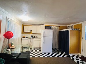A compact kitchen with a refrigerator, stove, and microwave. There is a glass table with a chair, and a checkered floor. - Cozy private studio.No pets. Near downtown (Chico)