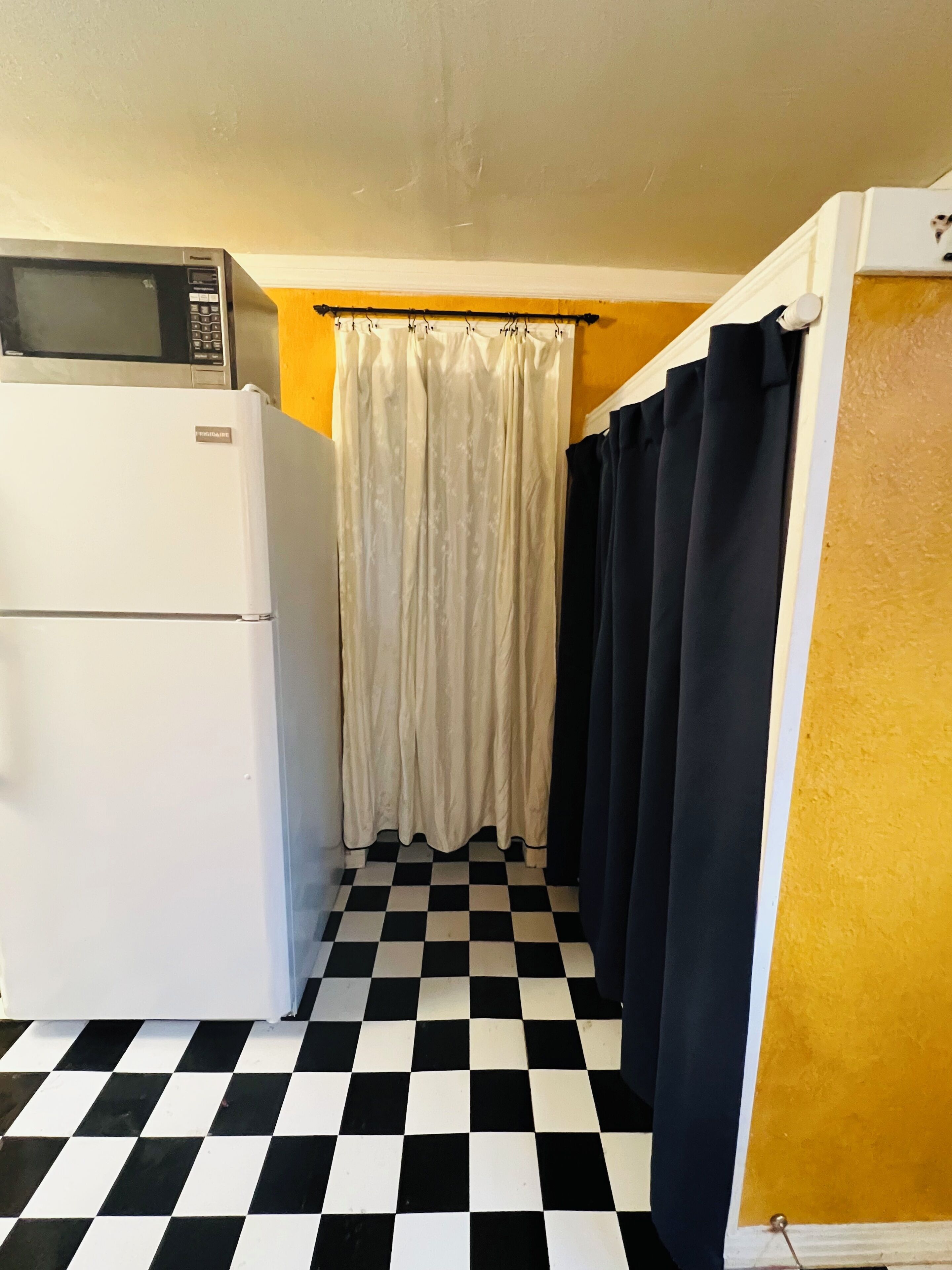 Een kleine keuken met een koelkast, magnetron en een zwart-wit geruite vloer.
