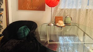 Una habitación con una mesa de vidrio, un florero rojo, una tetera verde y un cuadro en la pared.