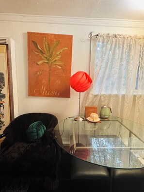 Ein Zimmer mit einem Glastisch, einer roten Blumenvase, einem grünen Teekännchen und einem Bild an der Wand.