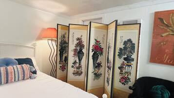 A bedroom with a bed, a lamp, a chair, and a decorative screen with artwork.