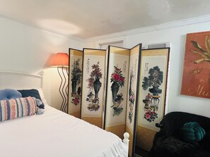 A bedroom with a bed, a lamp, a chair, and a decorative screen with artwork.