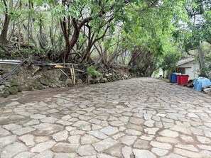 A cobblestone pathway in a wooded area with a small building and colorful trash bins. - Apartment # 1 Chi-ya, San Juan laguna (San Juan la laguna)