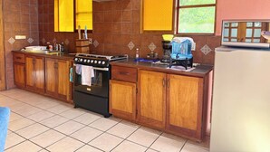 A kitchen with wooden cabinets, a stove, a sink, and a window with a view of greenery. - Apartment # 1 Chi-ya, San Juan laguna (San Juan la laguna)