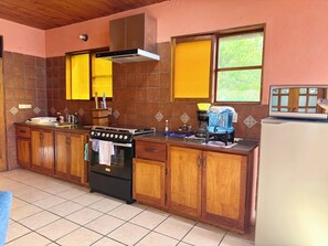 Uma cozinha com armários de madeira, fogão, pia e janela com vista para o verde.