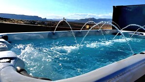 Ett bubbelbad med vattenstrålar, omgivet av en klar himmel och avlägsna berg.