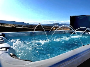 A hot tub with water jets, surrounded by a clear sky and distant mountains.