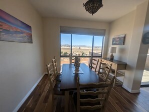 Un coin repas avec une table et des chaises, un tableau accroché au mur et une vue sur un paysage désertique, visible à travers de grandes fenêtres.