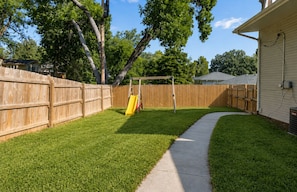A backyard with a wooden fence, a concrete path, and a yellow slide.