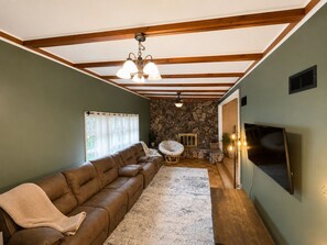 Una sala de estar con un sofá marrón, pared de piedra, vigas de madera, chimenea y televisor.